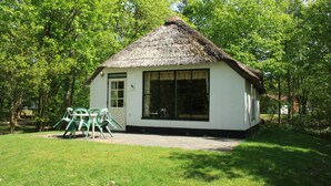 Une petite maison blanche au toit de chaume, entourée d’une végétation luxuriante.