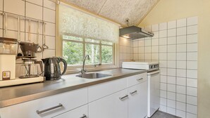 Une cuisine moderne avec des meubles blancs, un évier en acier inoxydable, une machine à café et une fenêtre donnant sur un paysage verdoyant.