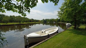 A narrow waterway with a small boat docked on the right, surrounded by lush greenery and trees. - Bungalow for 4 persons (Steendam)