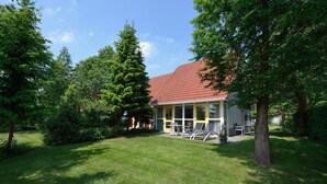A building with a red-tiled roof, surrounded by lush greenery and trees. - Bungalow for 4 persons (Steendam)