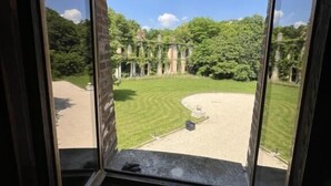Une pièce dotée d’une grande fenêtre en arc d’où l’on peut admirer un espace verdoyant parsemé de ruines et d’arbres.
