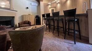 Un salon chaleureux avec une cheminée, un fauteuil en cuir et un coin bar avec des tabourets.