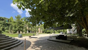 Une cour avec un chemin de gravier, un banc en bois et une sculpture en métal.