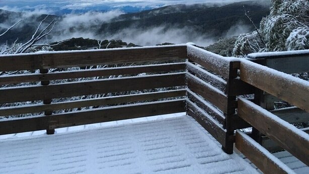 Un banco de madera con el suelo cubierto de nieve, con vistas a un paisaje montañoso y nublado.