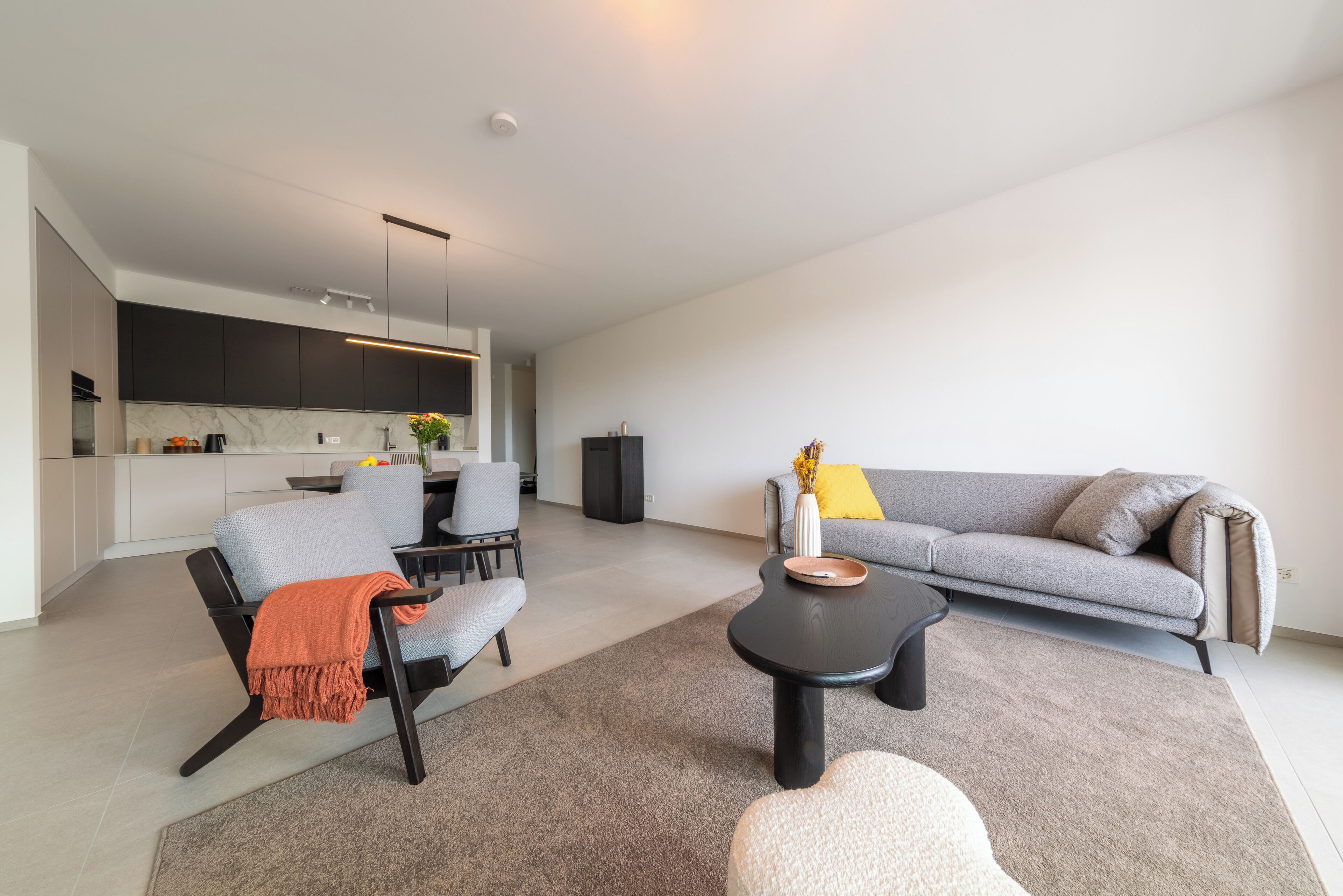 A modern living room with a grey sofa, a black coffee table, and a grey armchair with an orange throw.