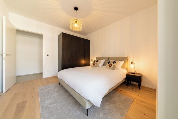 Une chambre à coucher avec un grand lit, une armoire, une table de chevet avec une lampe et un luminaire au plafond.
