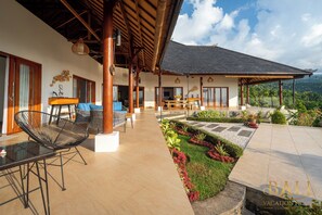 A spacious outdoor area with a covered seating area, a dining table, and a well-maintained garden with a stone pathway. - Villa Linggah Longgah, Bali - Spectacular Clifftop Elegance! (Kabupaten Buleleng)