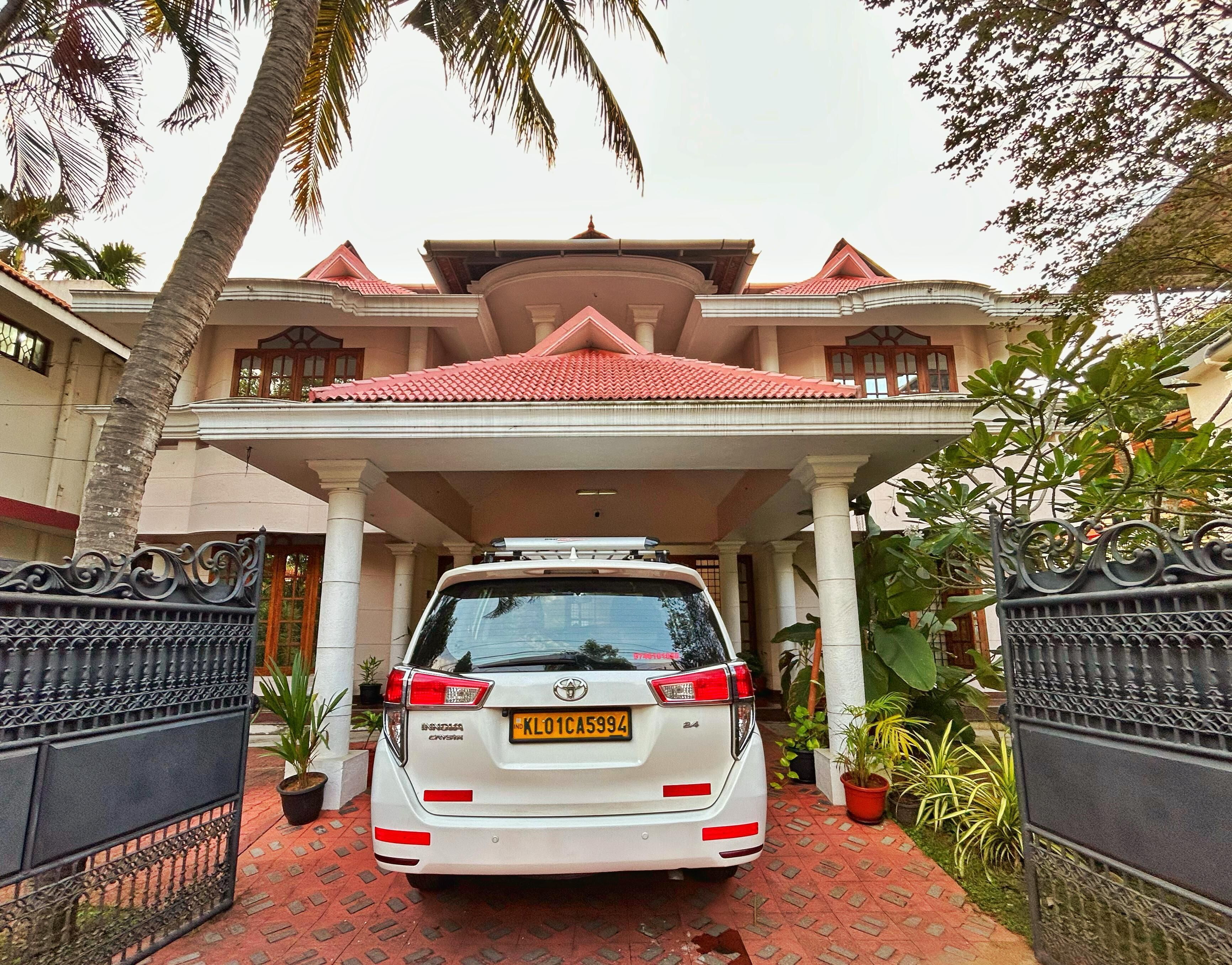 A white car parked in front of a house with a red-tiled roof, white columns, and a gated entrance.