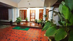 A spacious indoor area with a patterned floor, potted plants, and wooden doors. - La Casa Luxury AC Villa at Trivandrum City Centre, Just 5 min to Airport (Thiruvananthapuram)