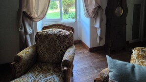 Une pièce comprenant un fauteuil à motifs, un canapé, une horloge et une fenêtre avec des rideaux.
