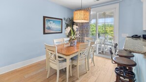 Un coin repas avec une table et des chaises en bois, un luminaire suspendu et une vue sur l’extérieur par une porte vitrée.