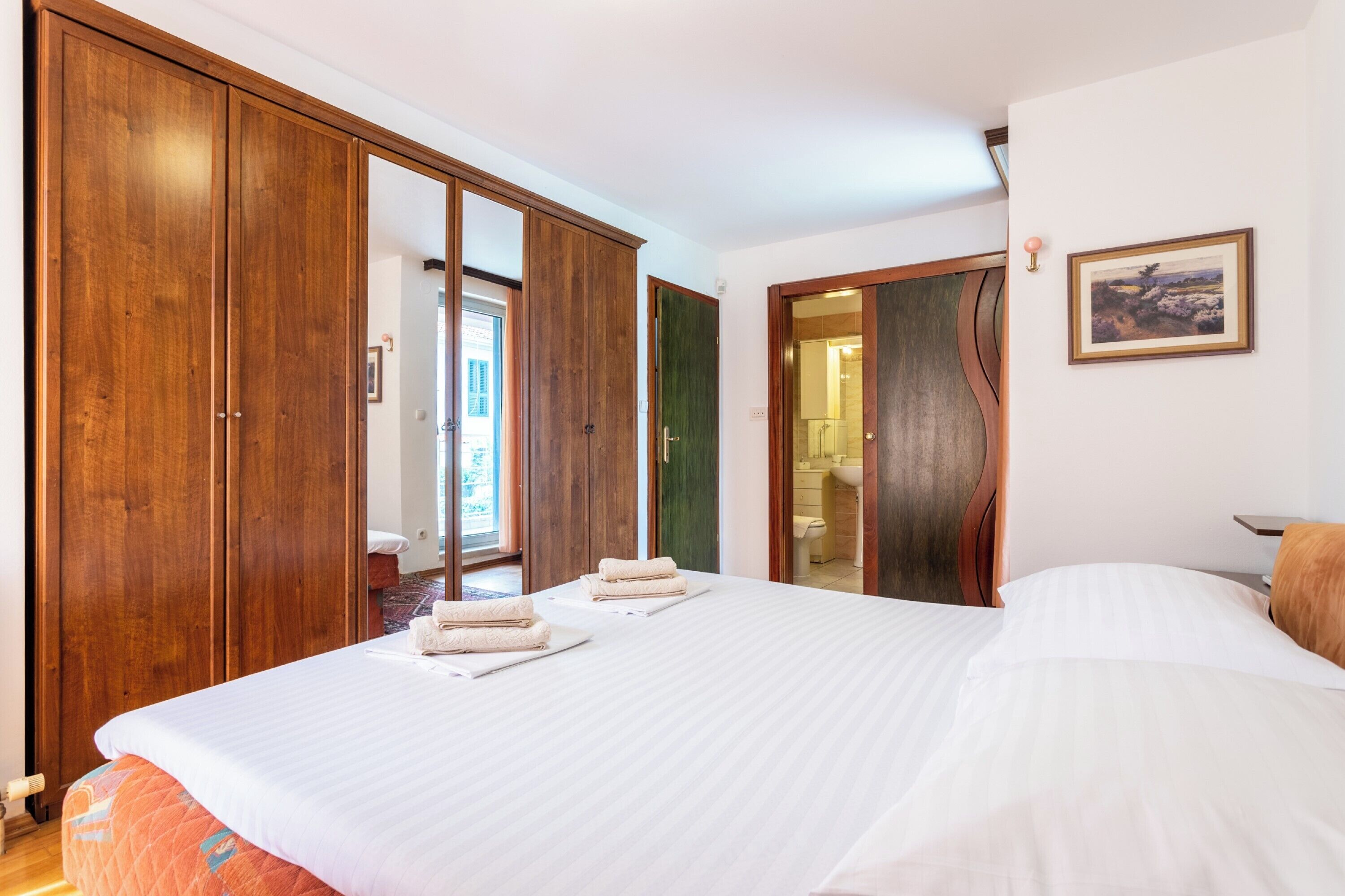 A hotel room with a large bed, wooden wardrobe, and a bathroom visible through an open door.
