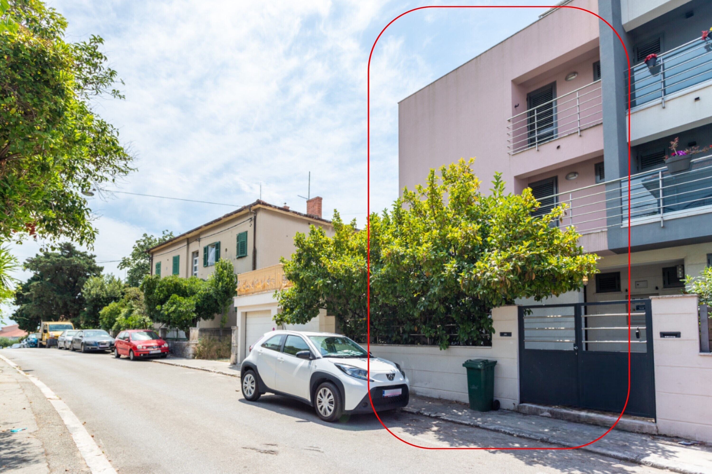 Une rue résidentielle bordée de voitures garées, avec un VUS blanc et un immeuble doté d’un balcon.