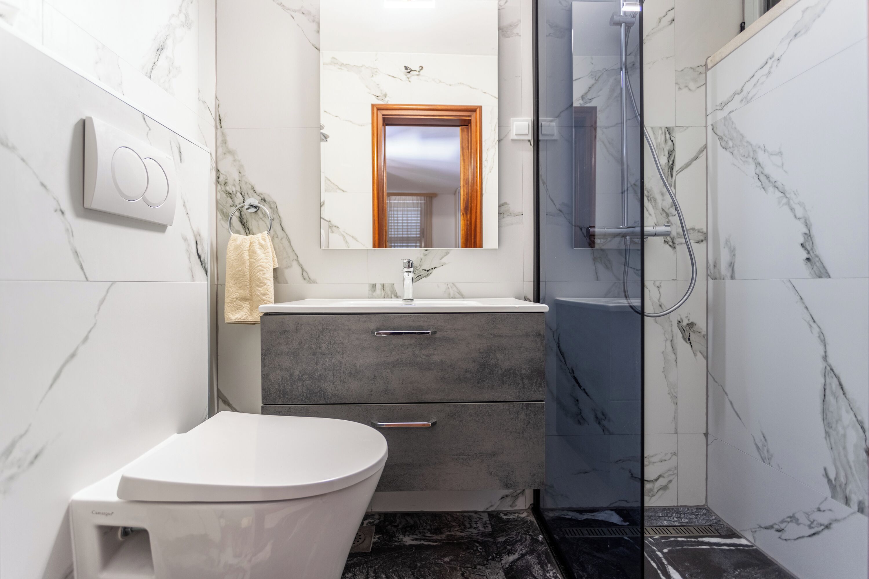 A modern bathroom with a white toilet, a grey vanity with a mirror, and a glass-enclosed shower area.