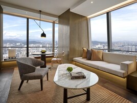 A modern living room with a sofa, chairs, a coffee table, and a view of a cityscape through large windows.