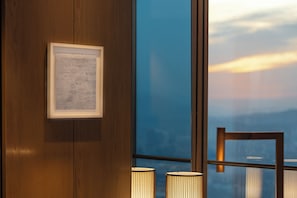 A framed text document on a wooden wall, a window with a view of the sky, and two cylindrical lamps.