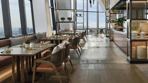 Een moderne eetruimte met hoge plafonds, grote ramen en uitzicht op de stad.