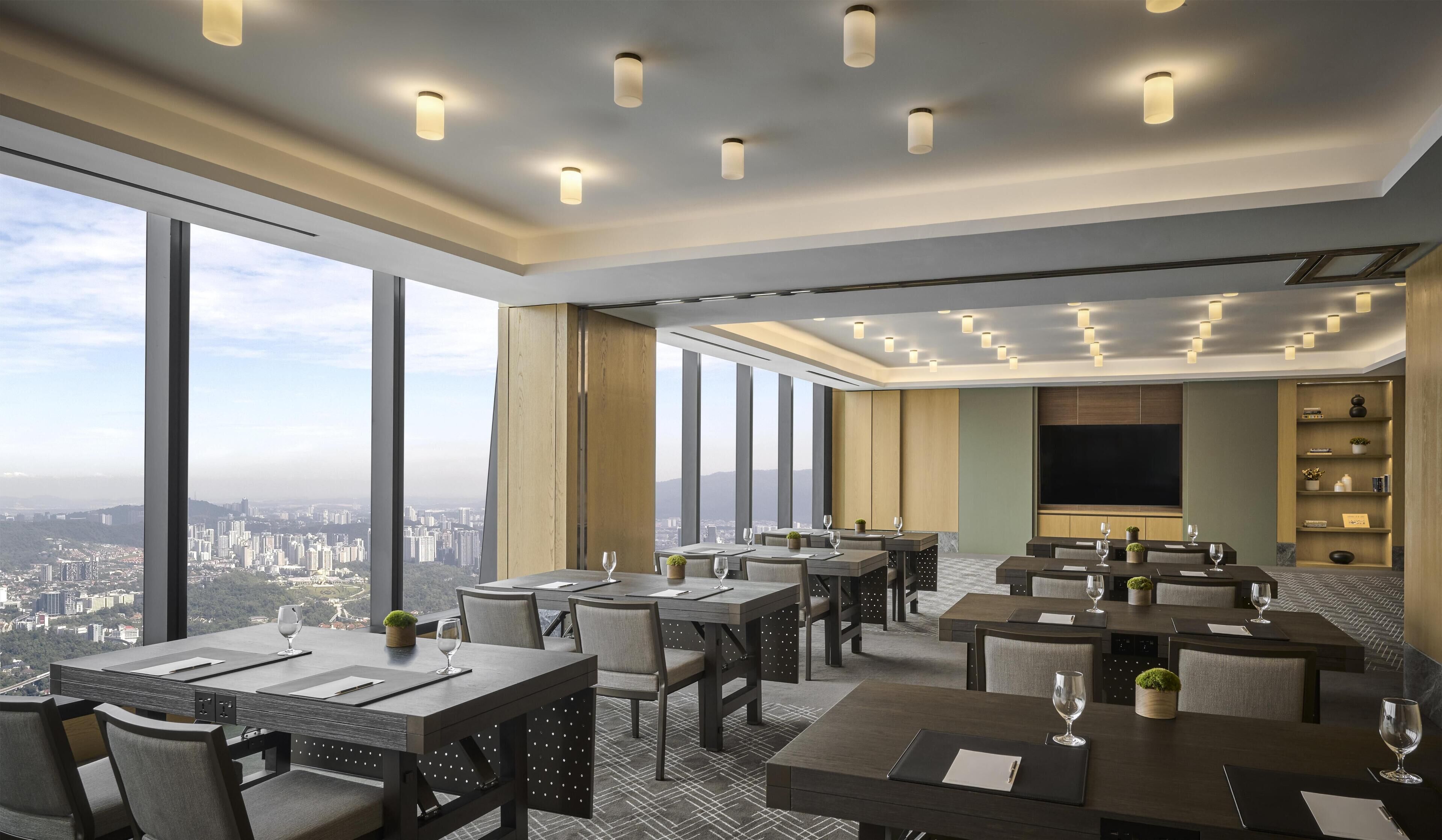 A modern hotel dining area with multiple tables, chairs, and a large TV screen.