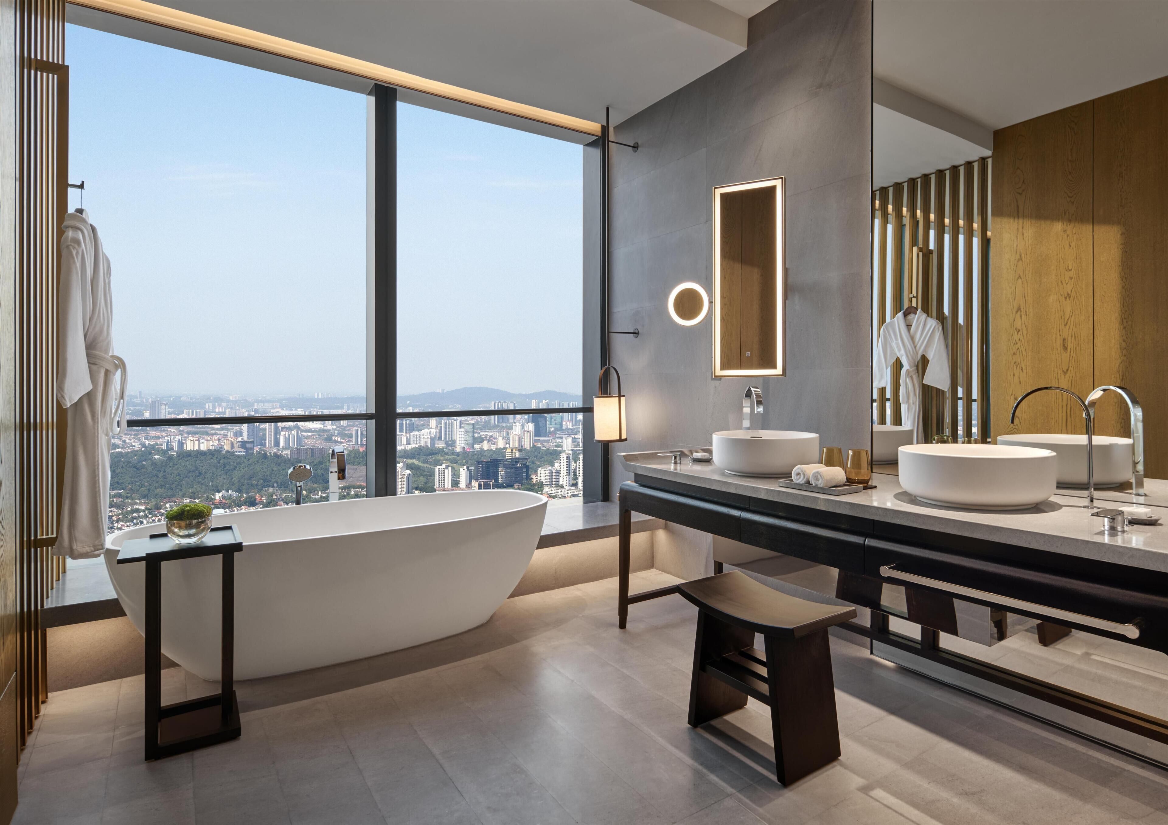 A modern bathroom with a freestanding bathtub, a large mirror, and a city view.