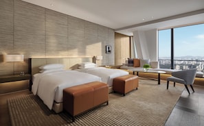 A modern hotel room with two beds, a seating area, and a large window offering a city view.