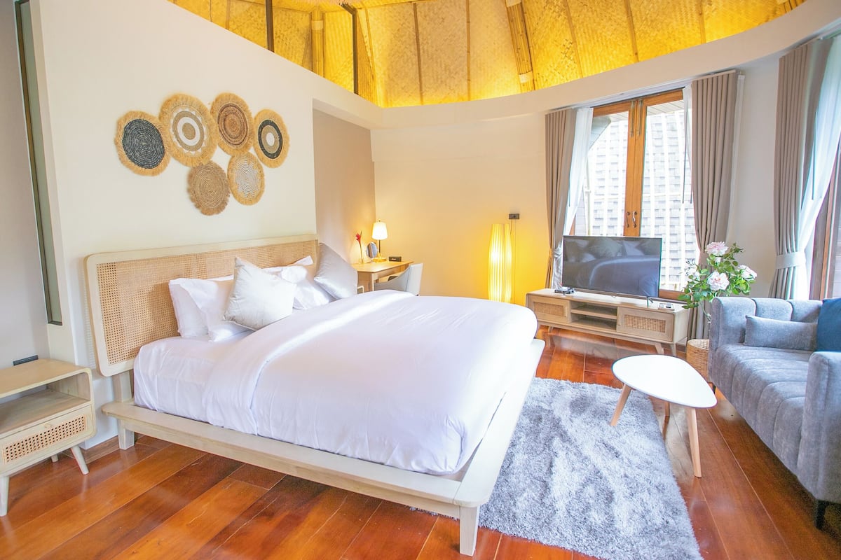A modern hotel room with a large bed, a desk, a TV, and a sofa.