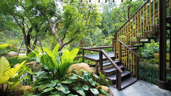A wooden staircase with a metal railing leading up to a platform surrounded by lush greenery and trees. - T-Story Maekampong (Mae On)