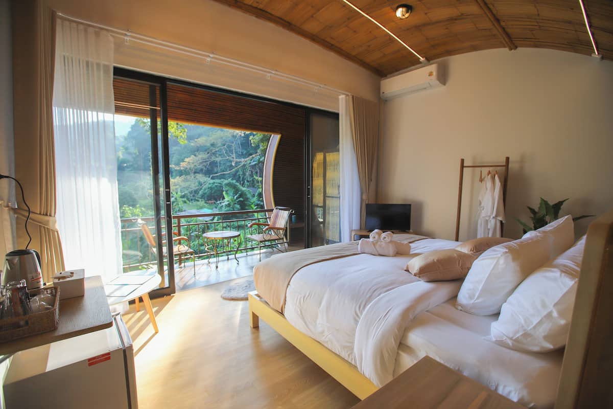 A bedroom with a large bed, a TV, and a balcony with a view of the outdoors.