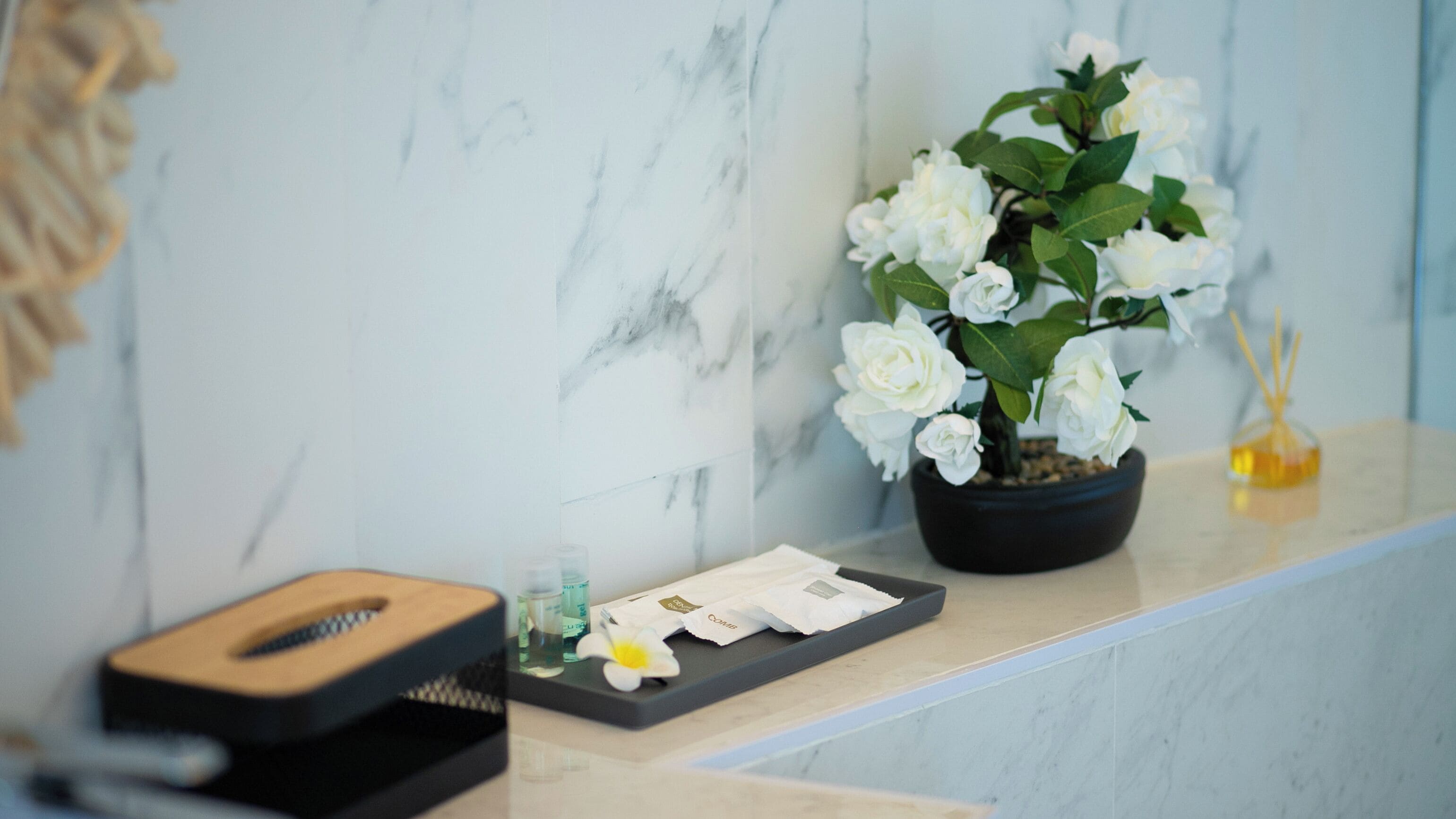 Una pared de mármol con una planta de rosa blanca en maceta y una pequeña botella de perfume sobre un mostrador.