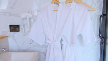 A bathroom with a marble wall, a sink, a hairdryer, and two white robes hanging on a rack.