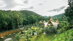 A traditional-style building with a thatched roof, surrounded by lush greenery and a small pond. - T-Story Maekampong (Mae On)