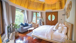 A spacious bedroom with a large bed, a sitting area with a sofa and a small table, and a wardrobe with a circular mirror. - T-Story Maekampong (Mae On)