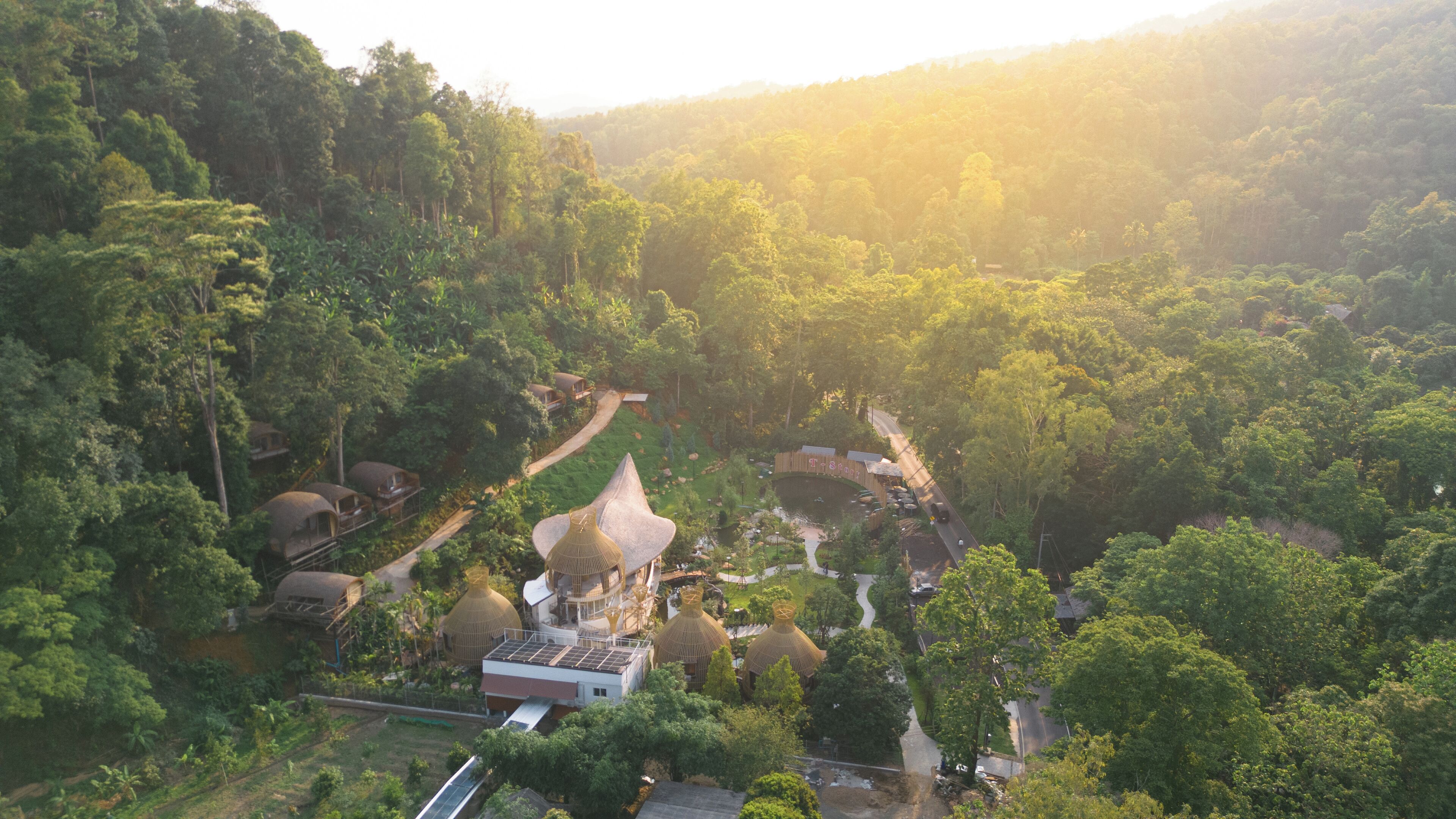 Vista aérea de un resort con múltiples alojamientos tipo bungalow, un edificio central con un techo cónico distintivo y un exuberante bosque circundante.