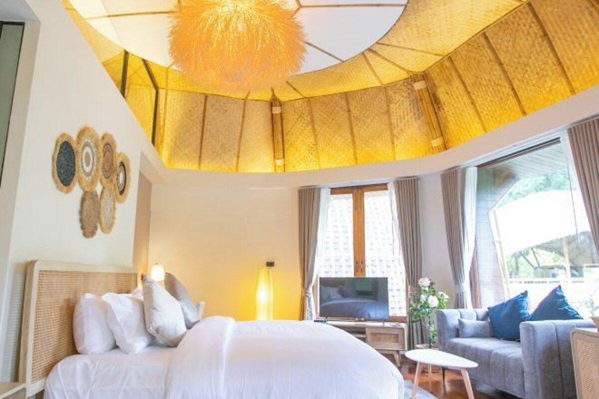 A hotel room with a bed, a sofa, a TV, and a large window with curtains.