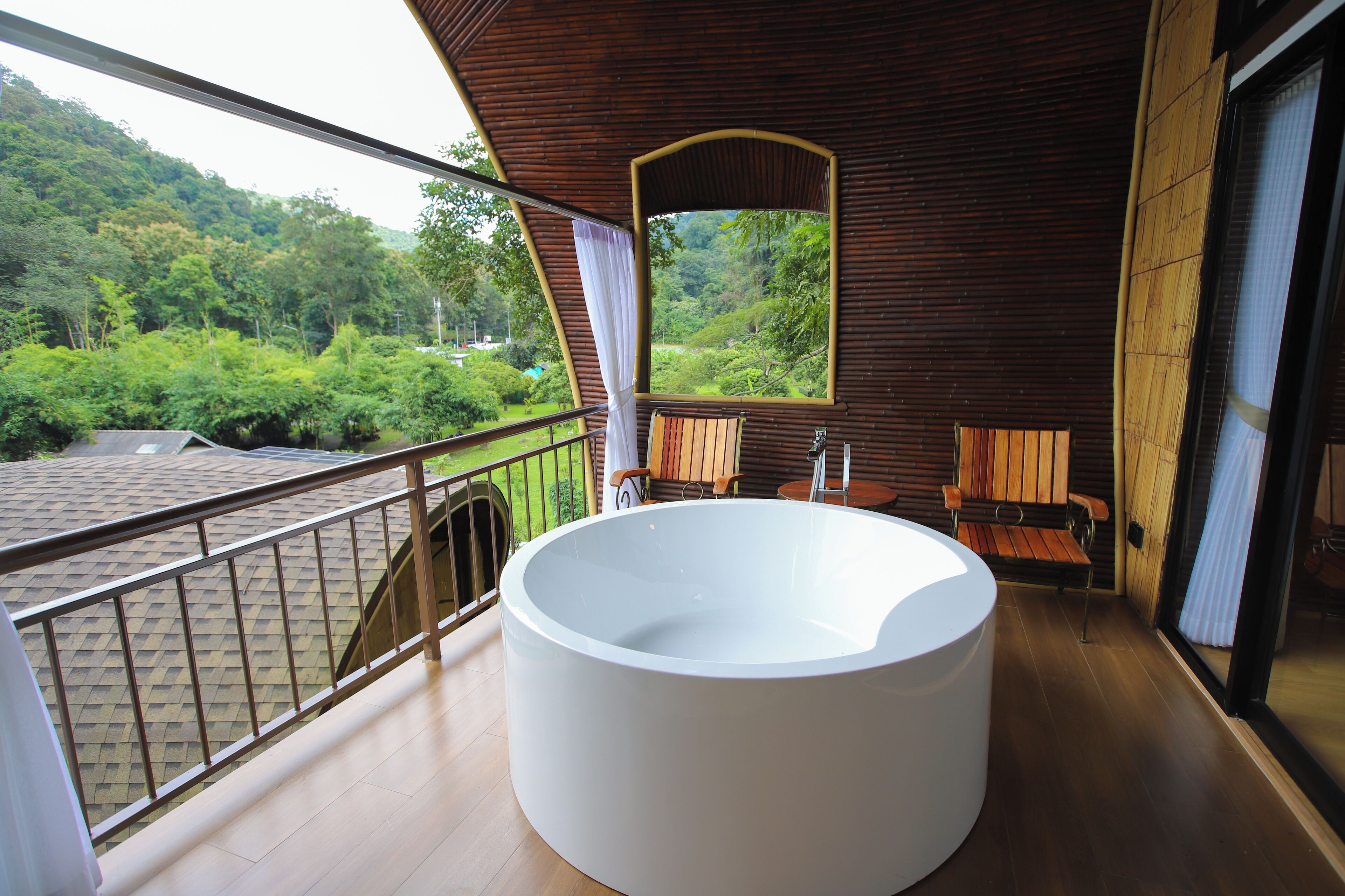 Un baño moderno con una bañera grande, paredes de madera y un balcón con vistas a un jardín exuberante.