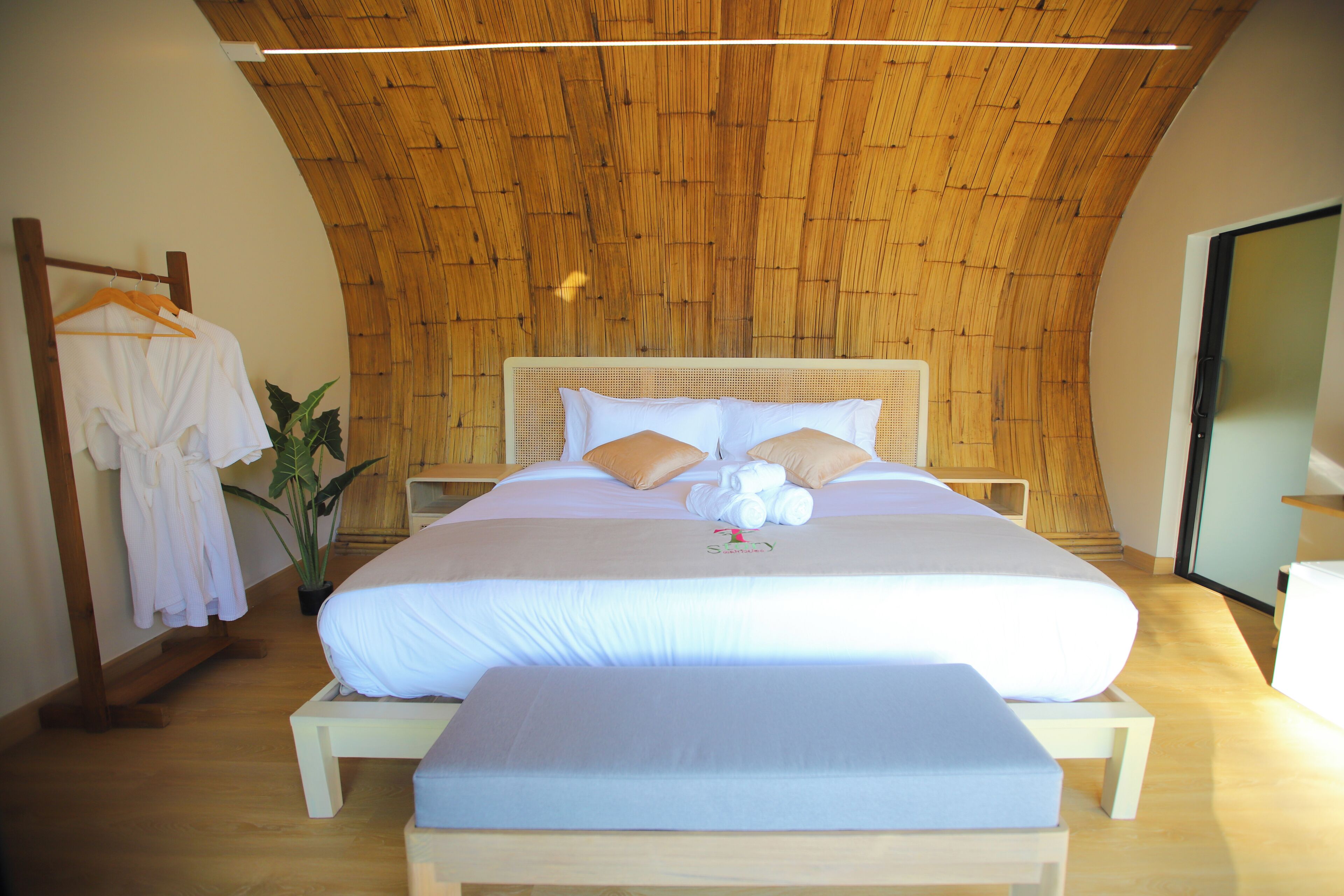 Ein Schlafzimmer mit einem großen Bett, Holzboden und einer Pflanze.