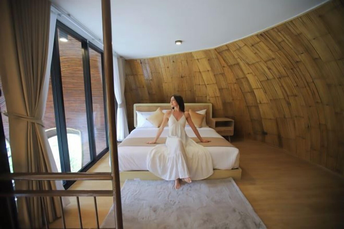 A spacious bedroom with a large bed, a wooden wall, and a view through a window.