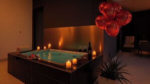 A modern spa room with a rectangular hot tub, candles, and a bottle of wine.
