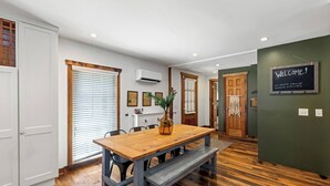 Un área de comedor con una mesa de madera y bancos, un florero con una planta, y un cartel que dice 'Welcome!' en la pared.