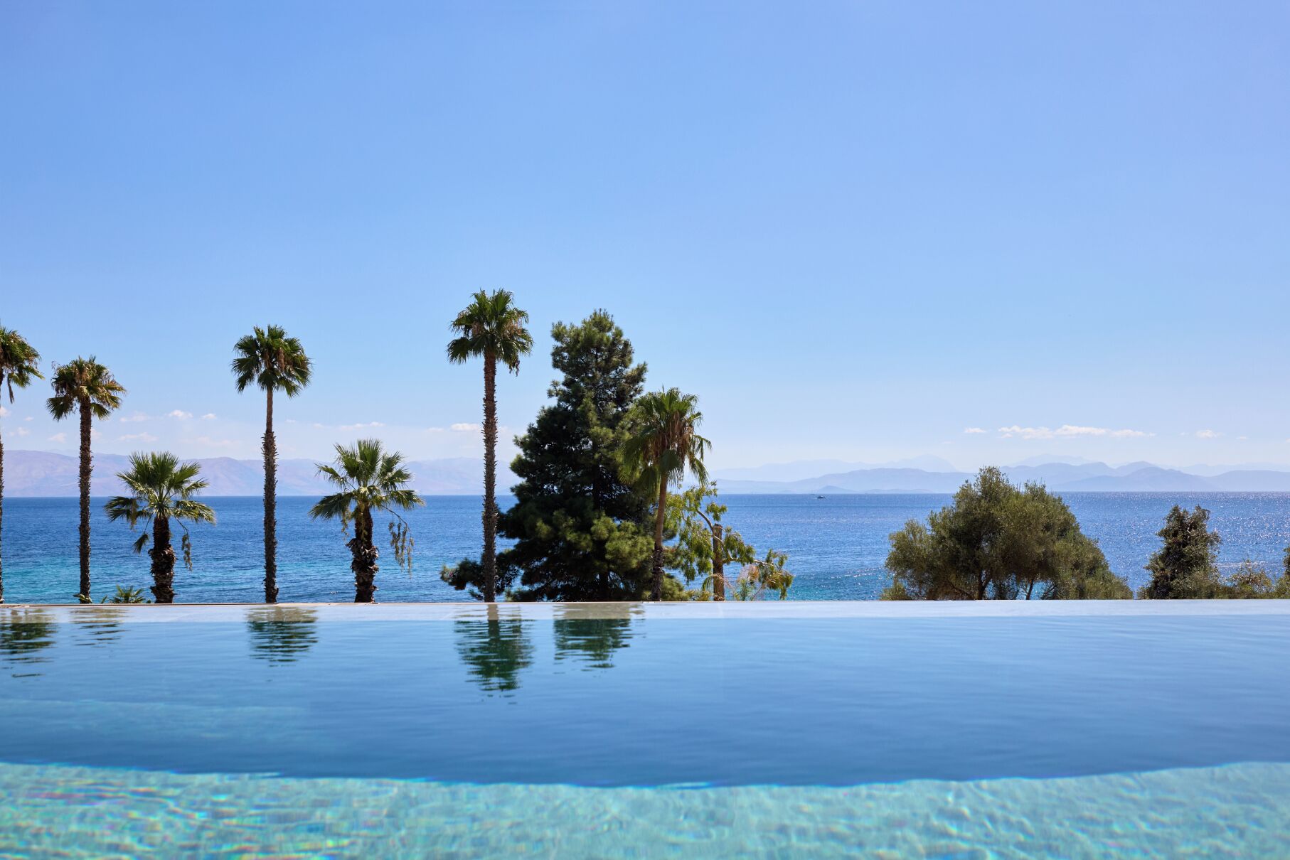Une piscine à débordement offrant une vue dégagée sur la mer et les montagnes en arrière-plan.
