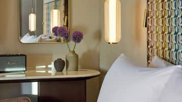 A hotel room with a bed, a bedside table with a radio, a vase with flowers, a mirror, and a patterned headboard.