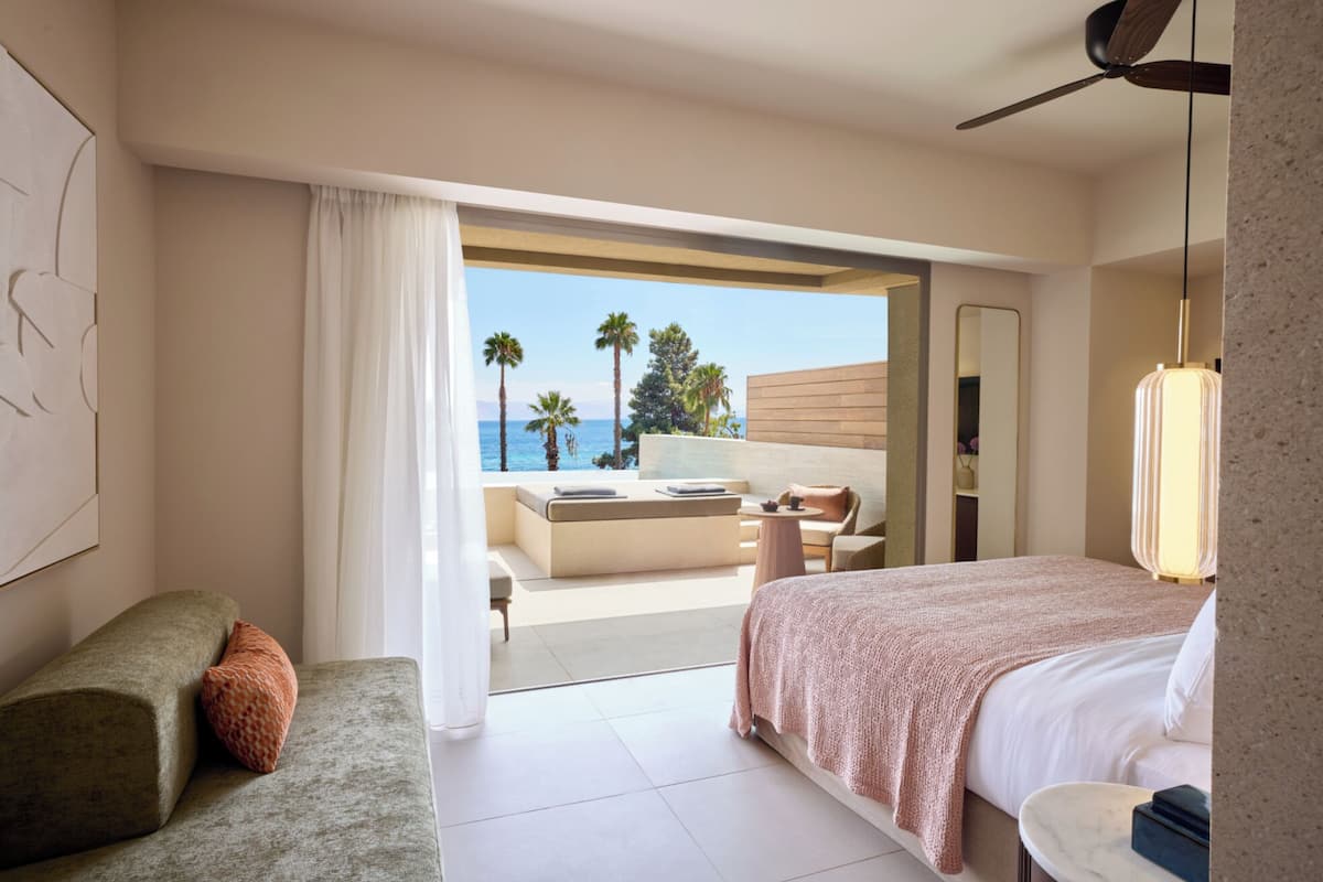 Une chambre d’hôtel comprenant un lit, un coin salon avec vue sur la mer, et un balcon avec une table et des chaises.
