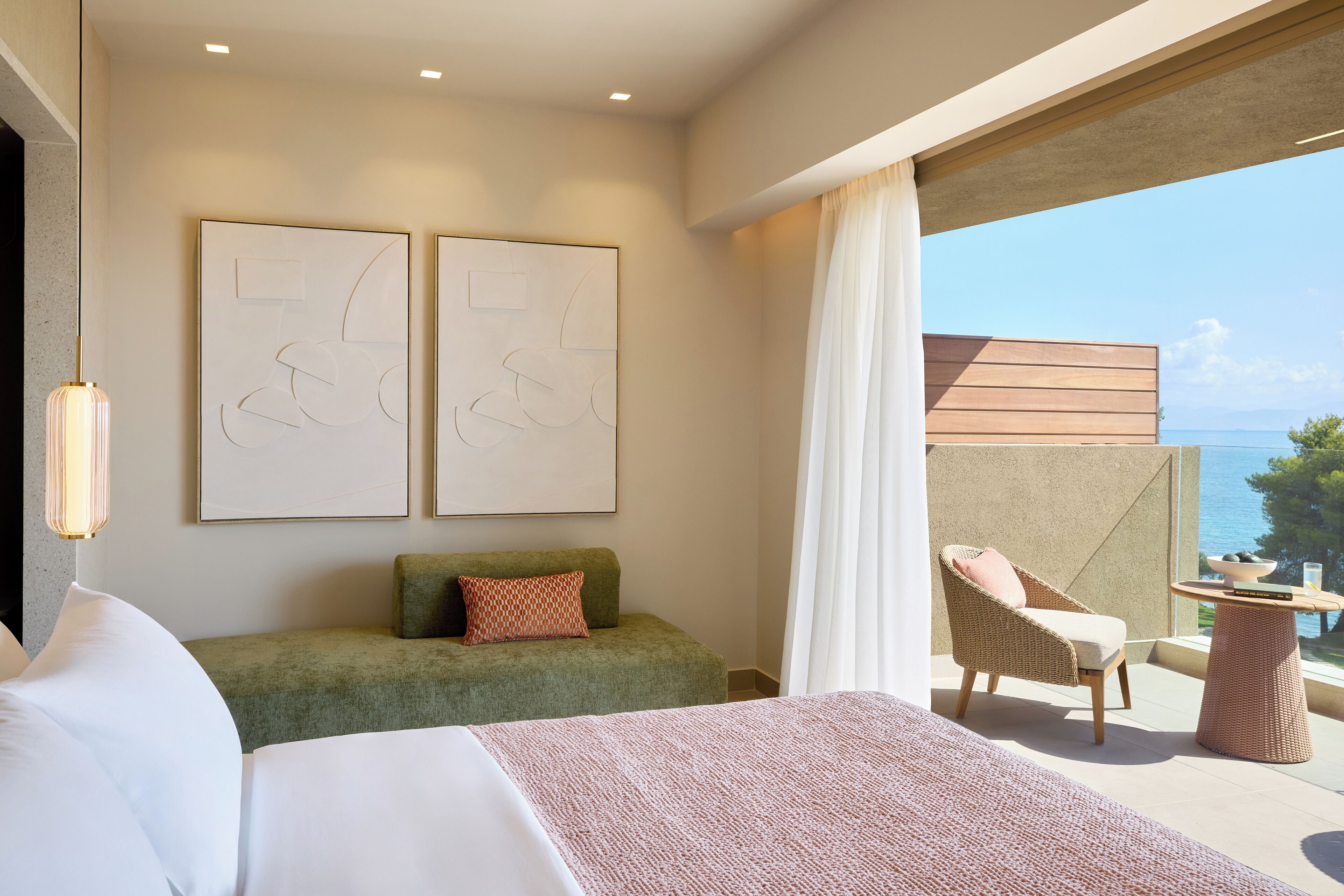 Habitación de hotel moderna con una cama grande, un sofá verde, un sillón de mimbre y un balcón con vistas al mar.