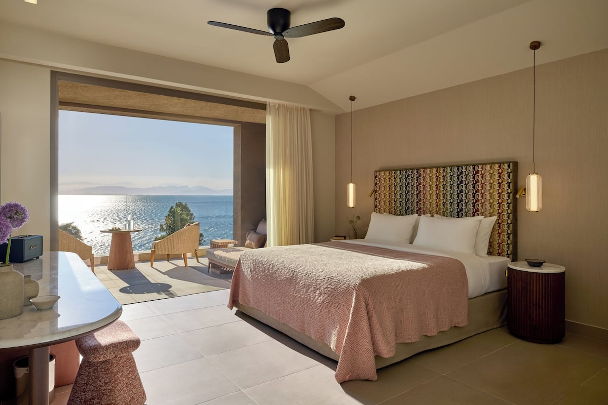 Une chambre d’hôtel moderne dotée d’un grand lit, d’un balcon avec vue sur la mer, d’un coin repas et d’un ventilateur de plafond.