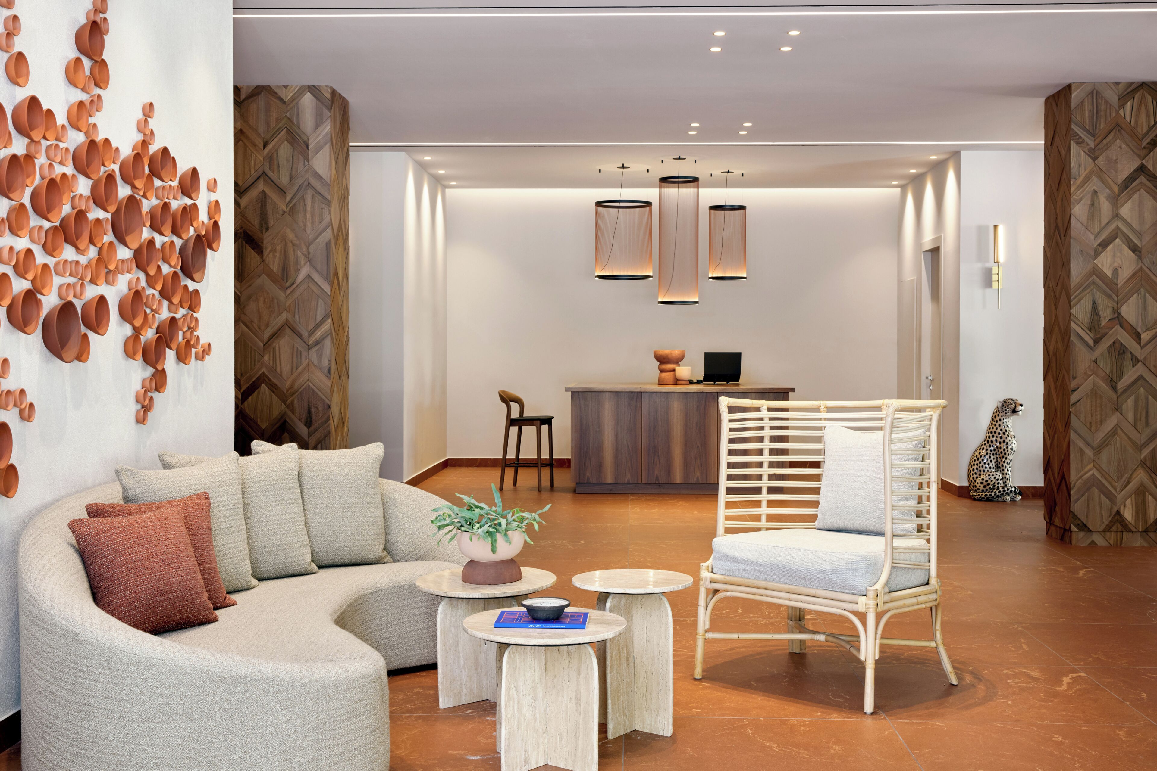 A modern interior with a curved sofa, a wicker chair, a small table with a plant, and a bar area in the background.