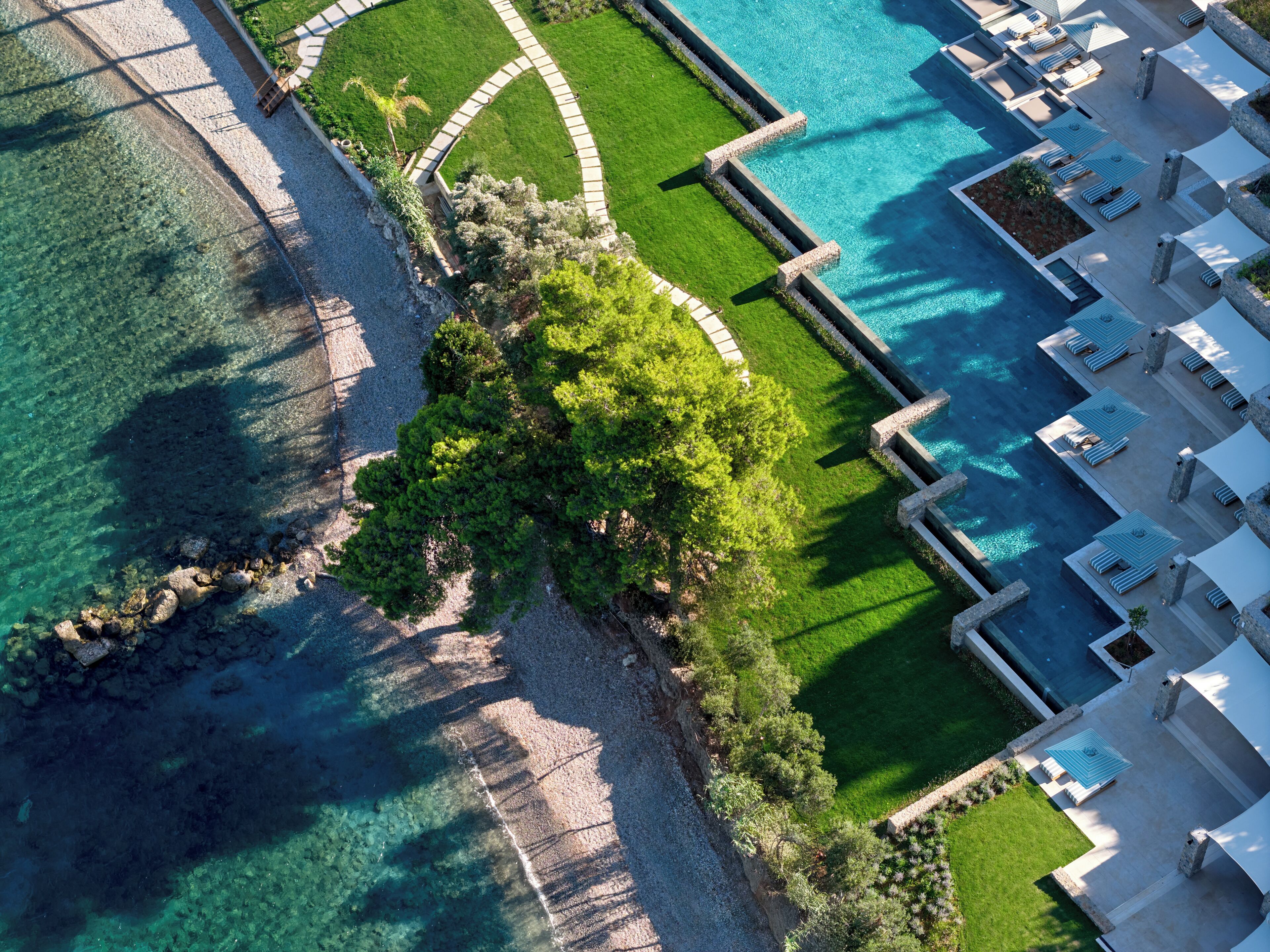 An aerial view of a resort with a swimming pool, lounge areas, and a landscaped garden.