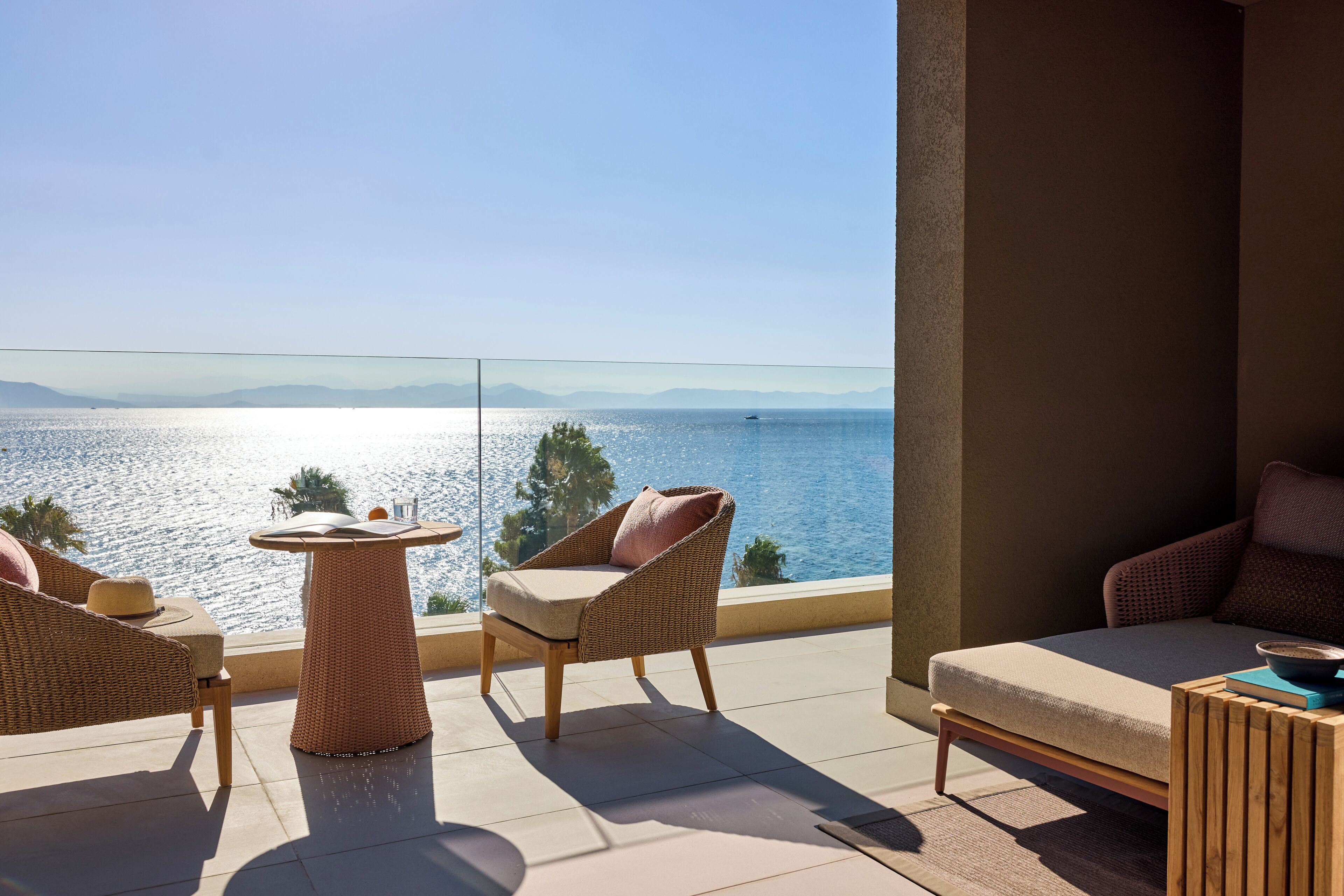 Un balcón con mobiliario de mimbre, una pequeña mesa y vistas al mar.