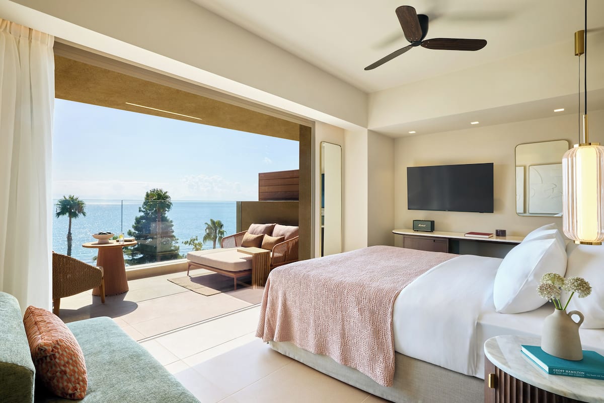 Une chambre d’hôtel moderne dotée d’un grand lit, d’un balcon avec vue sur la mer, d’une télévision à écran plat et d’un ventilateur de plafond.