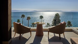 A balcony with wicker chairs and a small table, overlooking a body of water with palm trees and distant mountains. - Avali, Mar-Bella Collection (Corfu)