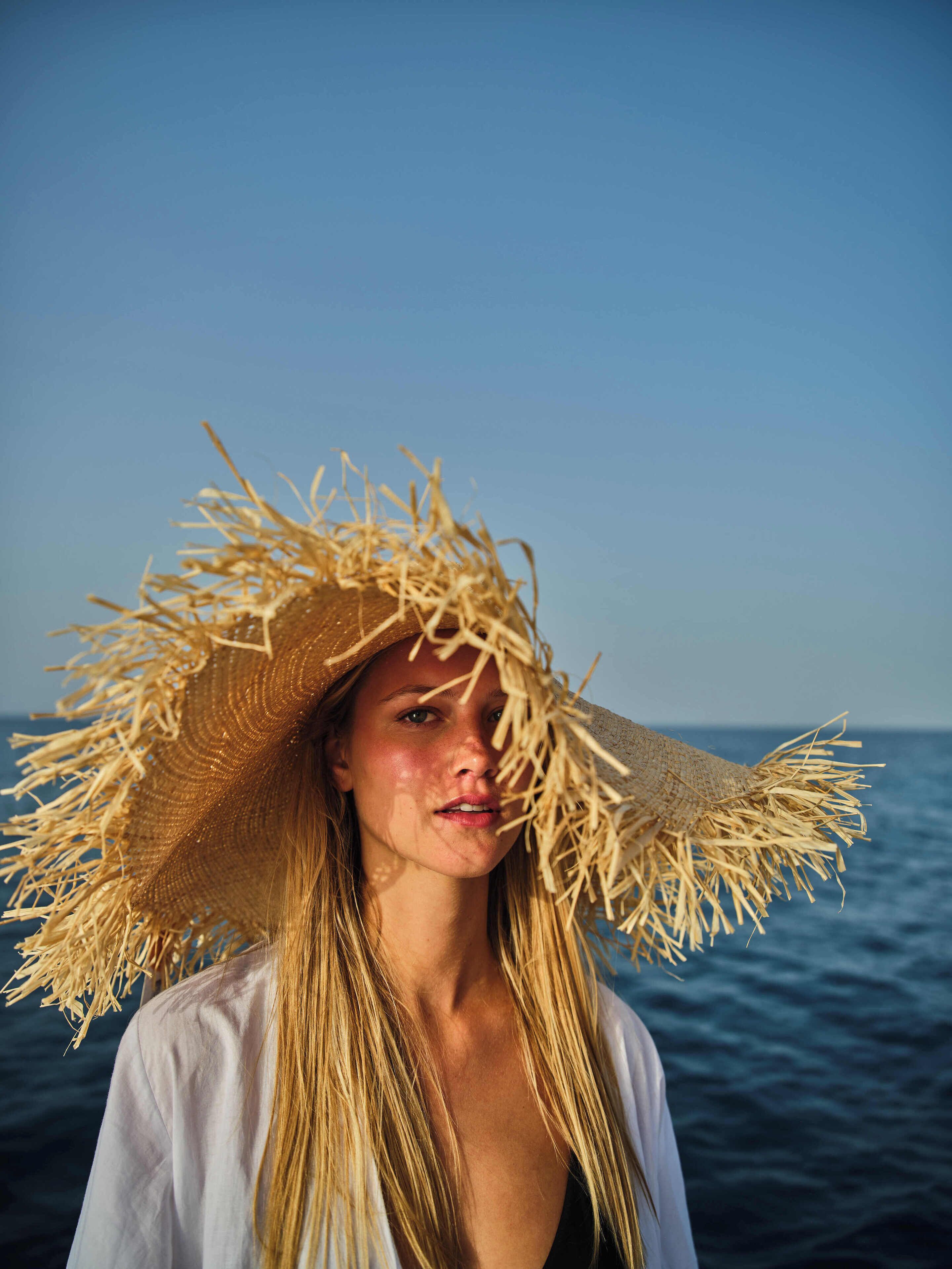 A person wearing a straw hat and a white shirt, standing by the sea.