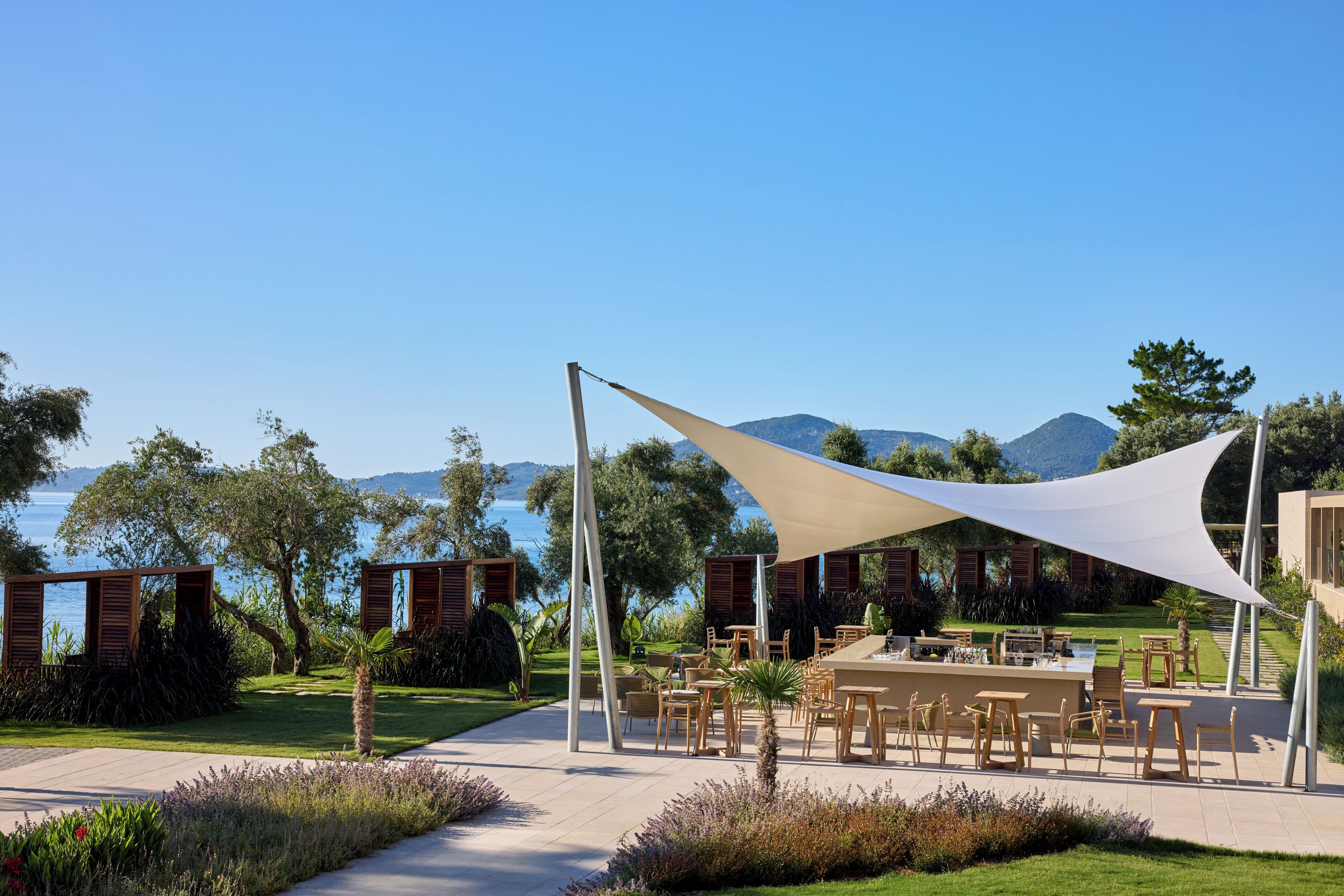 An outdoor dining area with tables and chairs, a white canopy, and a view of the sea and mountains.